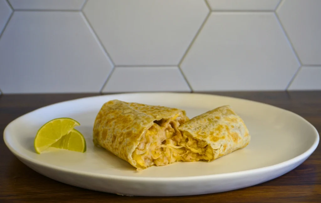 A burrito filled with cheese, accompanied by a lime wedge, served on a white plate.