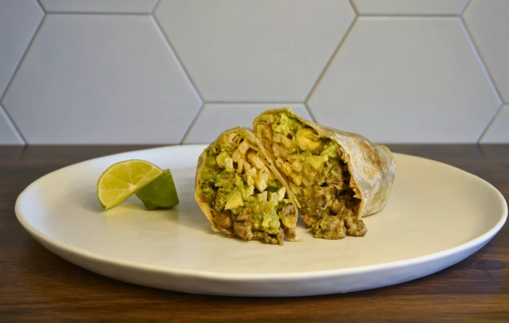 A burrito filled with avocado and meat, presented on a white plate.