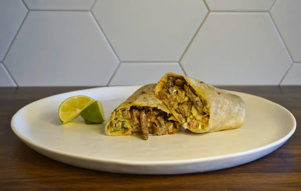 A burrito filled with meat and cheese, presented on a white plate.