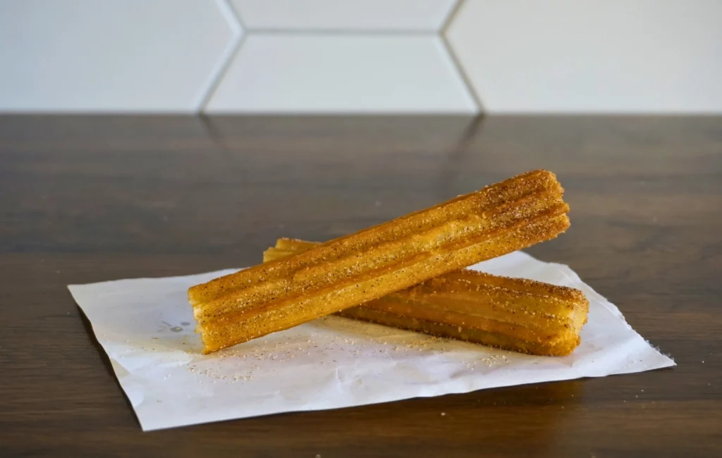 Two golden-brown churros placed on a white napkin, showcasing their crispy texture and sugary coating.