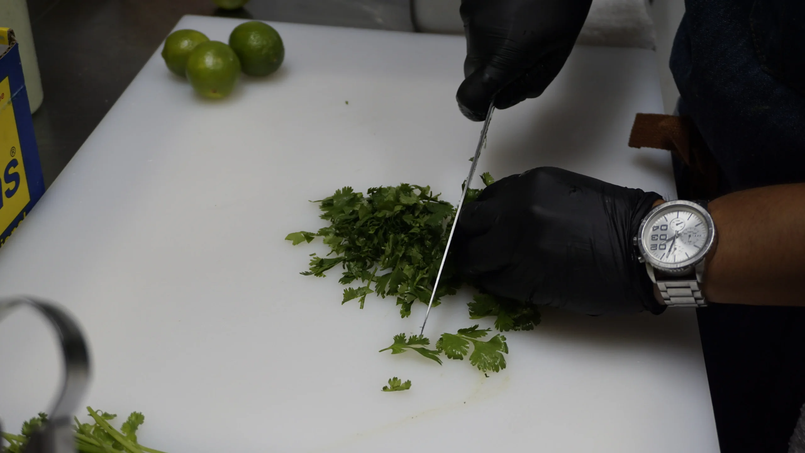A person using a knife to chop fresh green leaves on a cutting board.