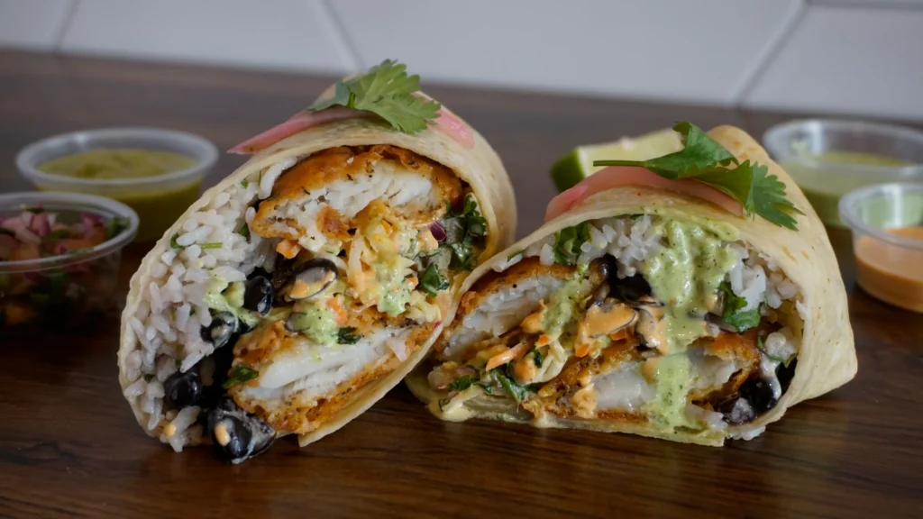 A fish burrito filled with rice and vegetables, placed on a rustic wooden table.