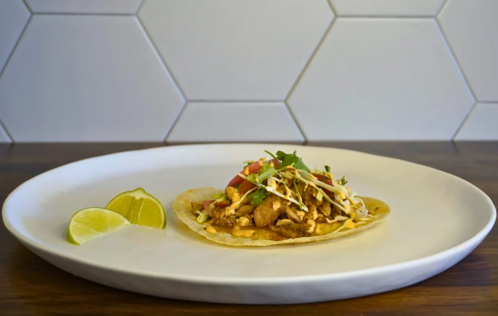 A taco on a white plate accompanied by fresh lime wedges for added flavor.