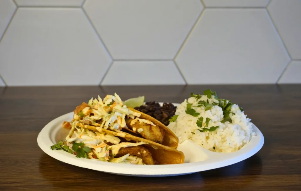 A plate featuring two tacos filled with ingredients and a serving of rice beside them.