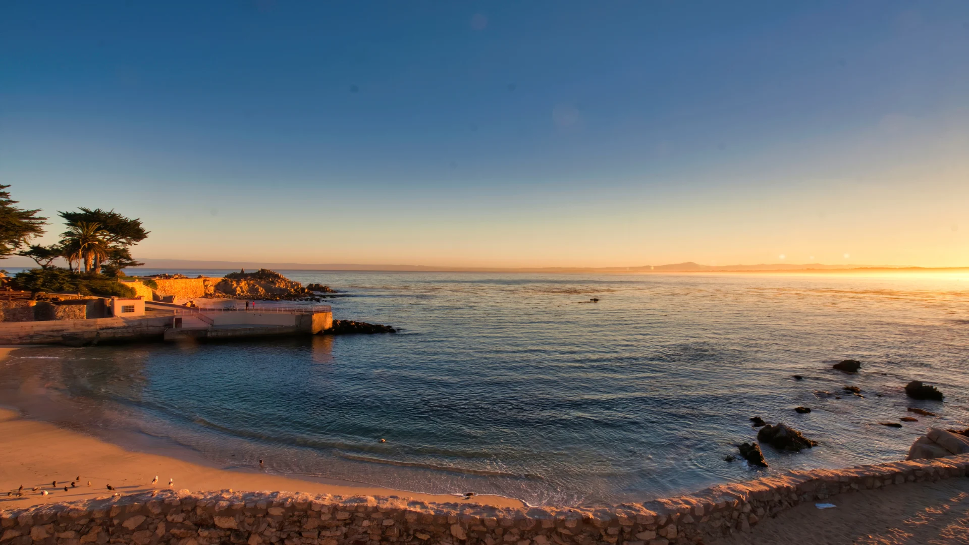 A vibrant sunset casts orange and pink hues over the ocean, reflecting on the calm waves and sandy beach.