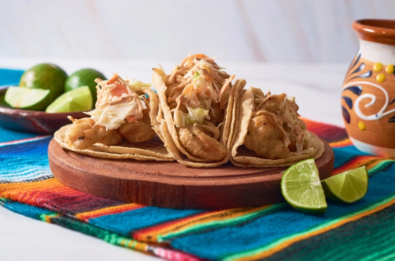 Three tacos on a wooden plate, accompanied by fresh lime wedges for added flavor.